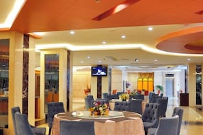 Un vestíbulo de hotel con una mesa redonda, asientos y una pantalla de televisión.