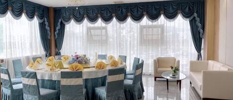 A round dining table with chairs, a chandelier, and curtains.