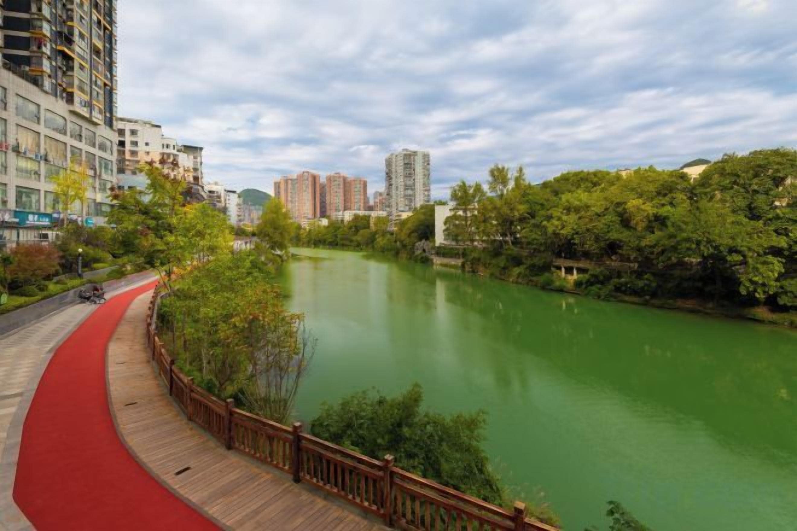 Un río con una pasarela de madera y un sendero rojo a su lado.