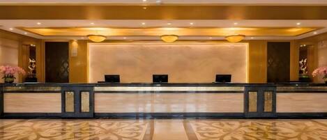Zona de recepción con mostrador de mármol, dos recepcionistas y suelo con diseño.