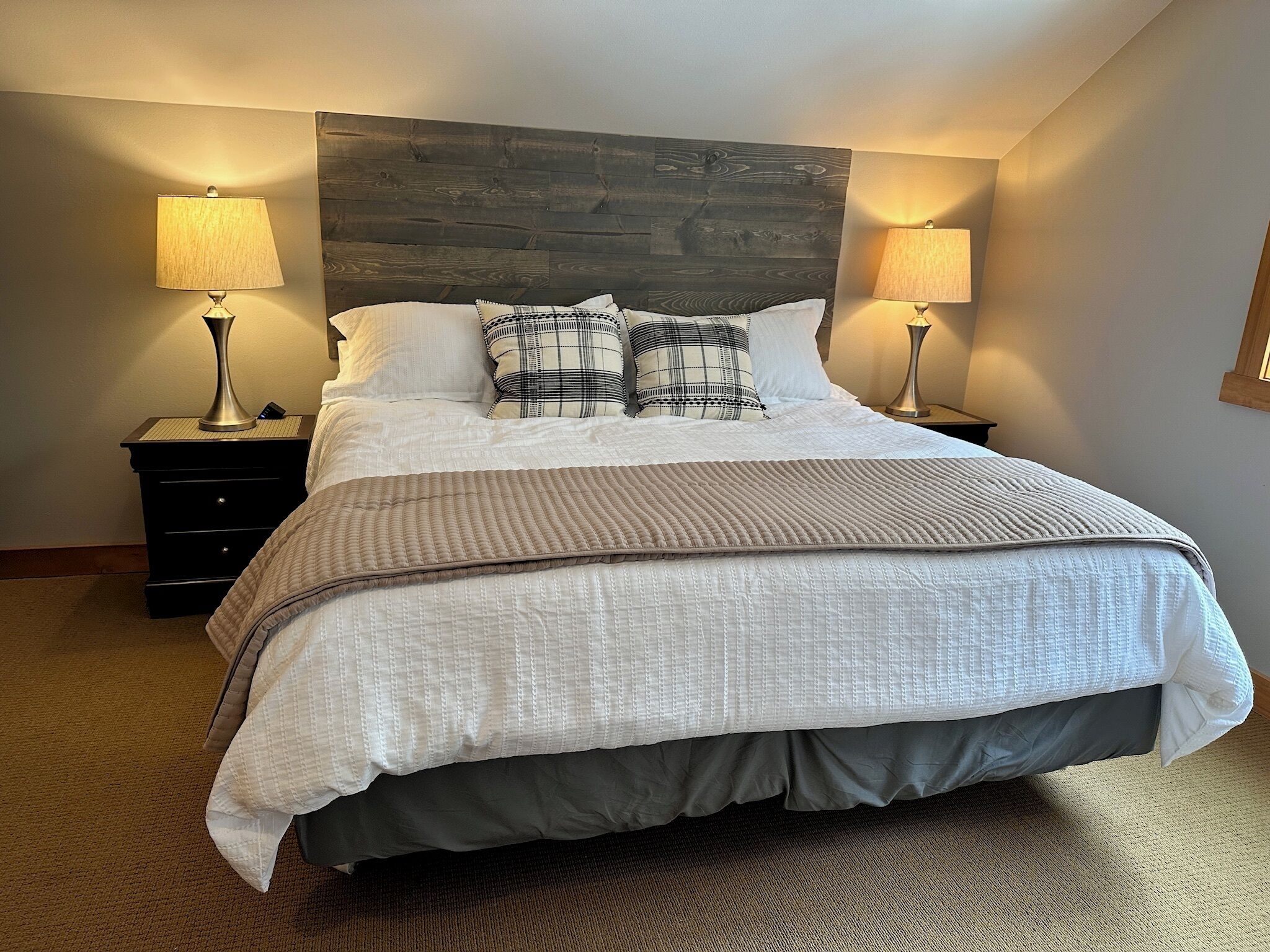 A neatly made bed with a wooden headboard, two bedside lamps, and a patterned throw blanket.