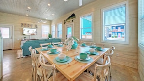 A dining area with a wooden table, chairs, and a view of the outside. - Sleeps 24, 2 Homes Pool, Backyard Tiki Bar, Fire Pit, Cornhole Walk to Beach (Port Aransas)