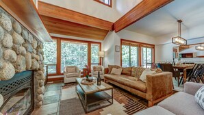 A spacious living room with a fireplace, large windows, and a dining area. - Large 3BD Village Townhome (Whistler)