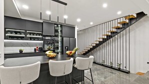 A modern kitchen with a central island, bar stools, and a staircase with wooden steps. - Villa Mosaicus with Pool (Makarska)