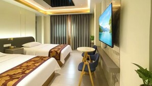 Ett hotellrum med två sängar, en tv, ett litet runt bord och en växt.