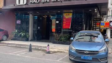Fachada de hotel con un coche azul estacionado frente a un hidrante y un cartel.