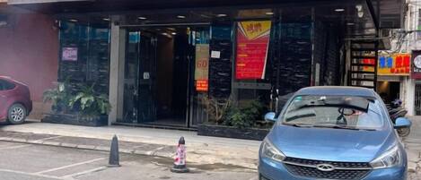 L’entrée d’un hôtel, avec une voiture bleue garée devant, un potelet d’hydrant et un panneau indicateur.