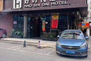 A hotel entrance with a blue car parked in front, a fire hydrant, and a signboard. - Haoshidai Hotel (Nanning Jiangnan Passenger Station Jinxiang Avenue Subway Station) (Nanning)
