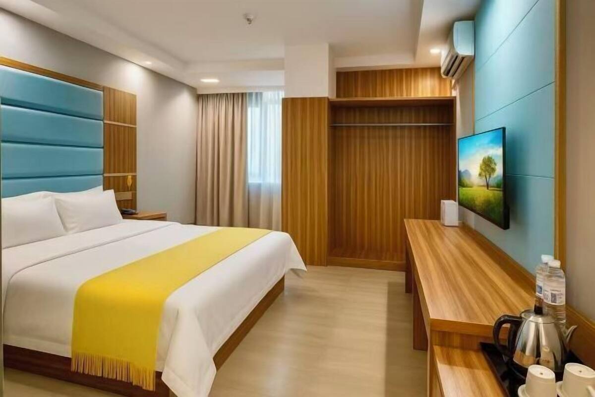 A hotel room with a large bed, a wooden desk, a television, and a window with curtains.