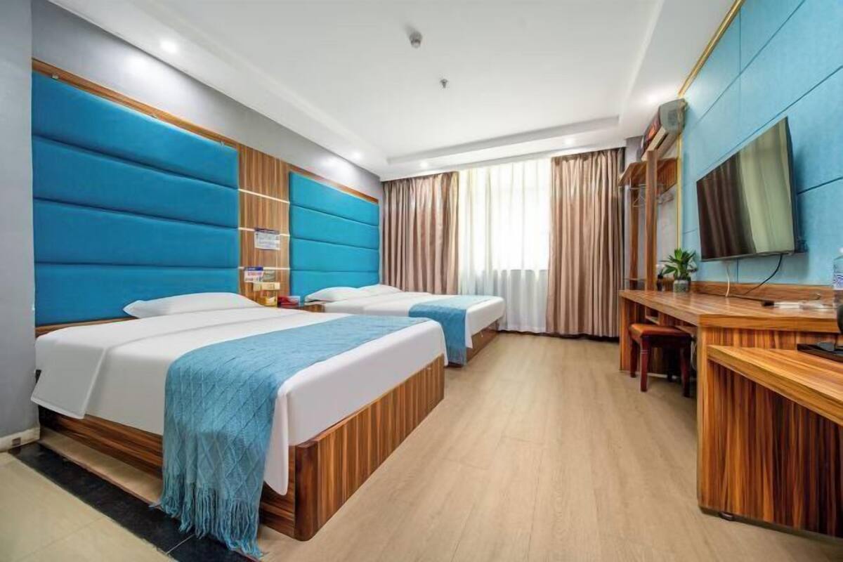 A hotel room with two beds, a desk, a TV, and a window with curtains.