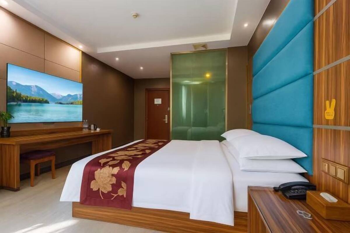 A modern hotel room with a large bed, a desk, a television, and a view of a mountain landscape.