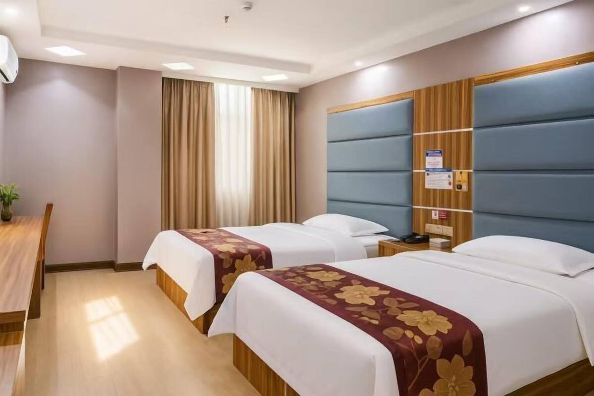 A hotel room with two beds, a desk, and a window with curtains.