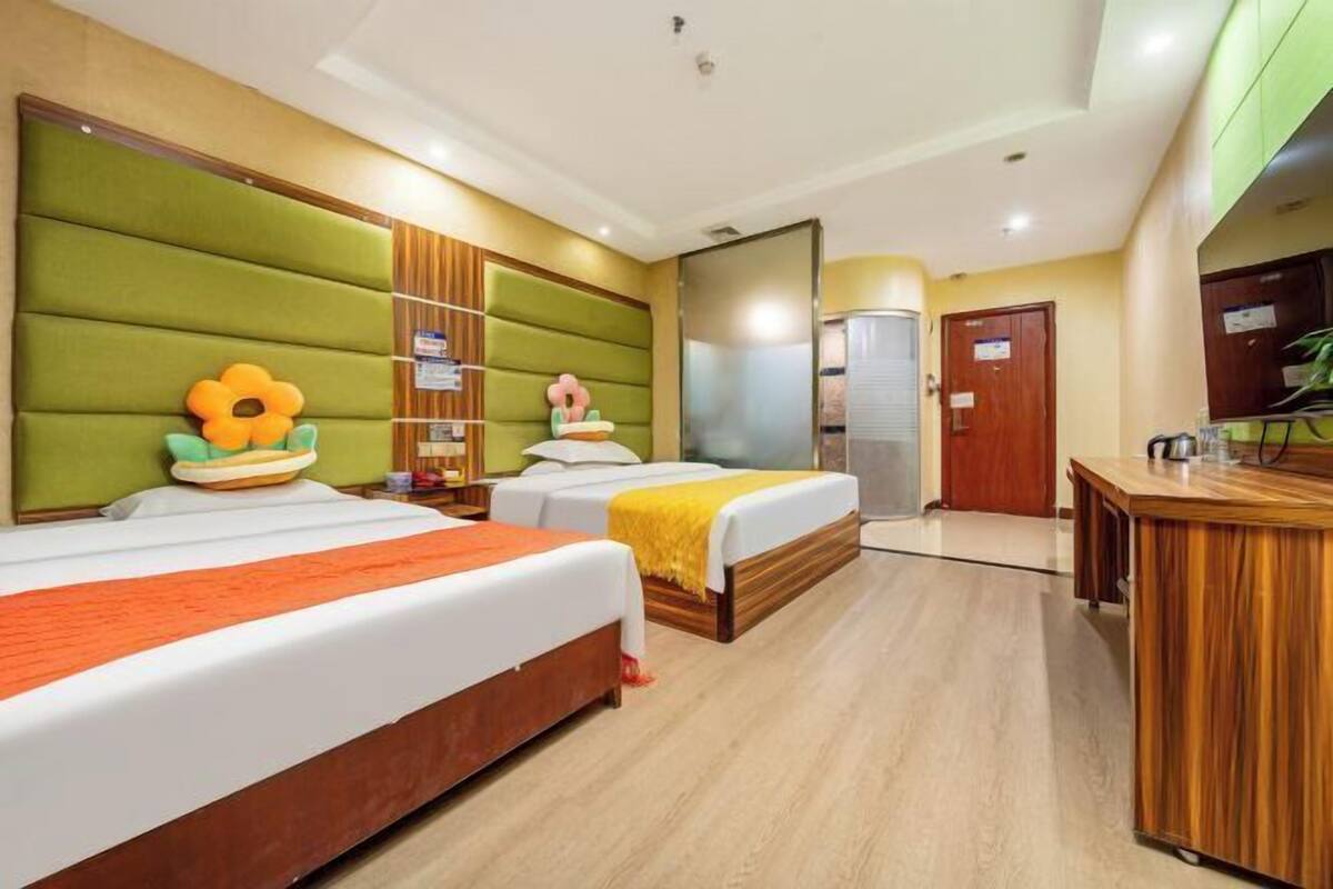A hotel room with two beds, a wooden desk, and a green padded headboard.