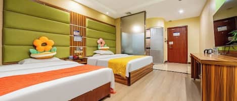 A hotel room with two beds, a wooden desk, and a green padded headboard.