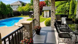 A covered patio with a pool, stone pillars, outdoor furniture, and a view of the backyard.