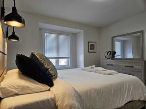 A bedroom with a bed, a dresser, a mirror, and a window with blinds. - Windsor Luxury Stay Oasis (Windsor)
