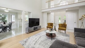 A spacious living area with a high ceiling, a dining area, and a staircase leading to an upper level.