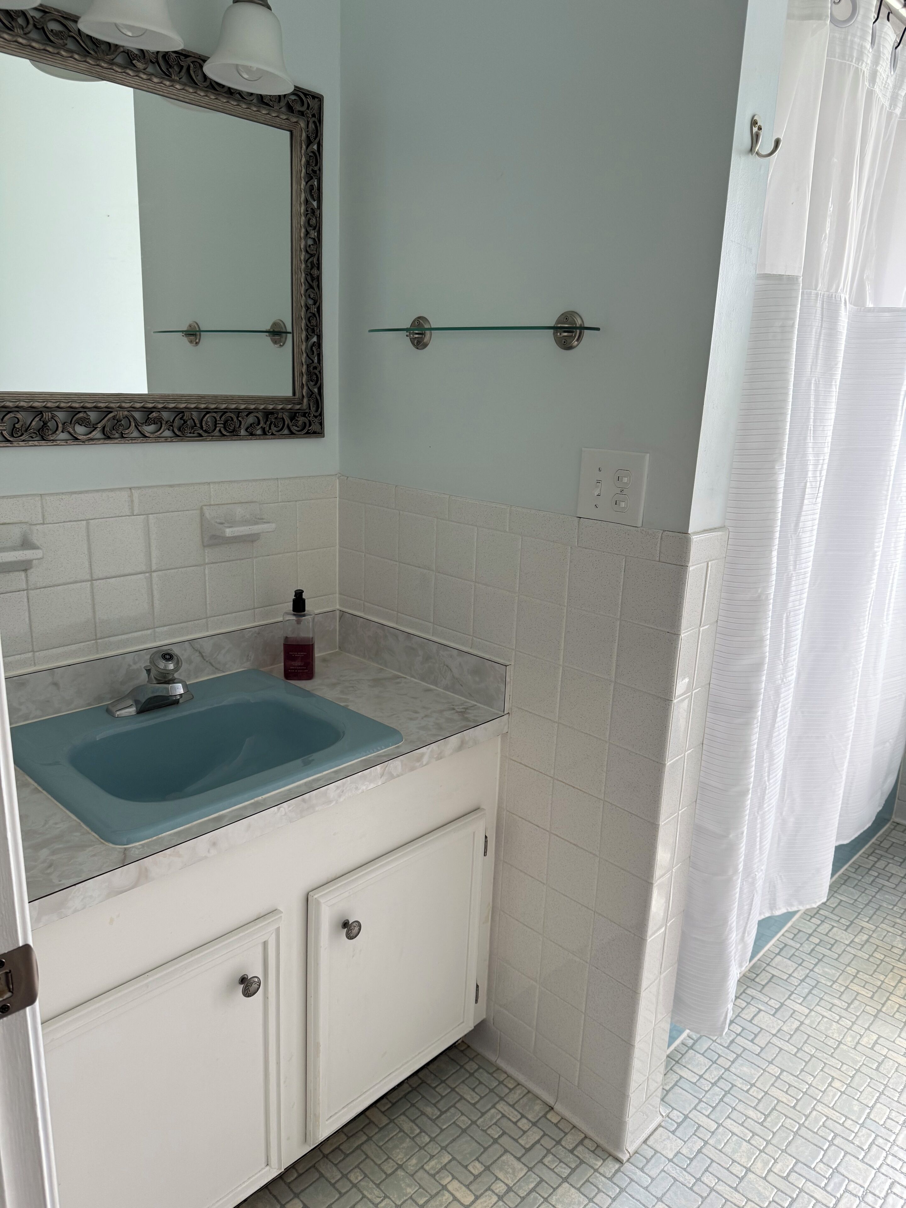 A bathroom with a blue sink, white cabinets, a mirror with an ornate frame, and a shower curtain.