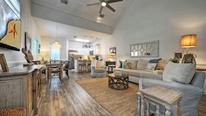 A spacious living room with a large sofa, a dining area with a wooden table, and a kitchen in the background. - Sleeps 29, 3 Homes Beachside Resort Pool, Walk to the Beach (Port Aransas)