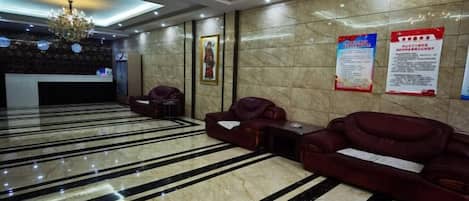 Un hall de hotel con suelo de mármol, sofás rojos, un mostrador de recepción y una araña.