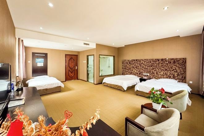 A hotel room with three beds, a desk with a computer, a TV, and a decorative plant.
