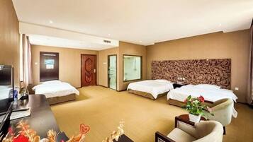 A hotel room with three beds, a desk with a computer, a TV, and a decorative plant.