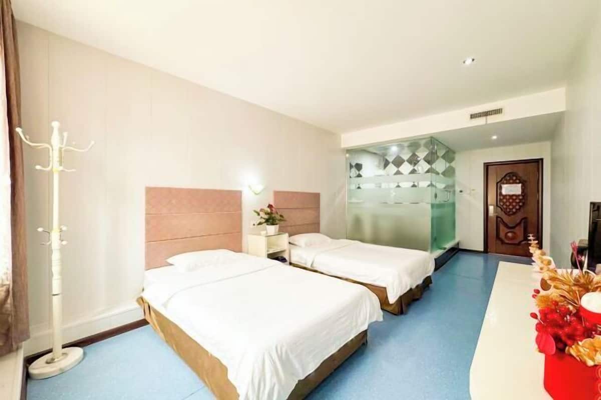 Quarto de hotel com duas camas, um cabideiro, uma mesa pequena com uma planta e uma decoração na parede.