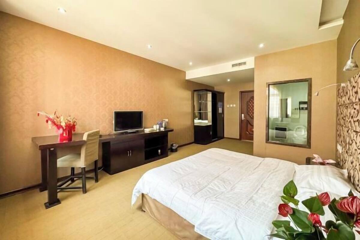 Quarto de hotel com cama, escrivaninha, cadeira, televisão e espelho.
