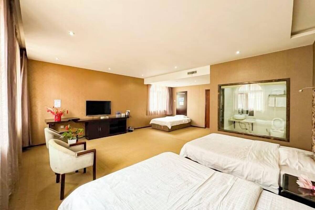 Quarto de hotel com duas camas, uma escrivaninha com televisão, uma cadeira e uma janela grande.