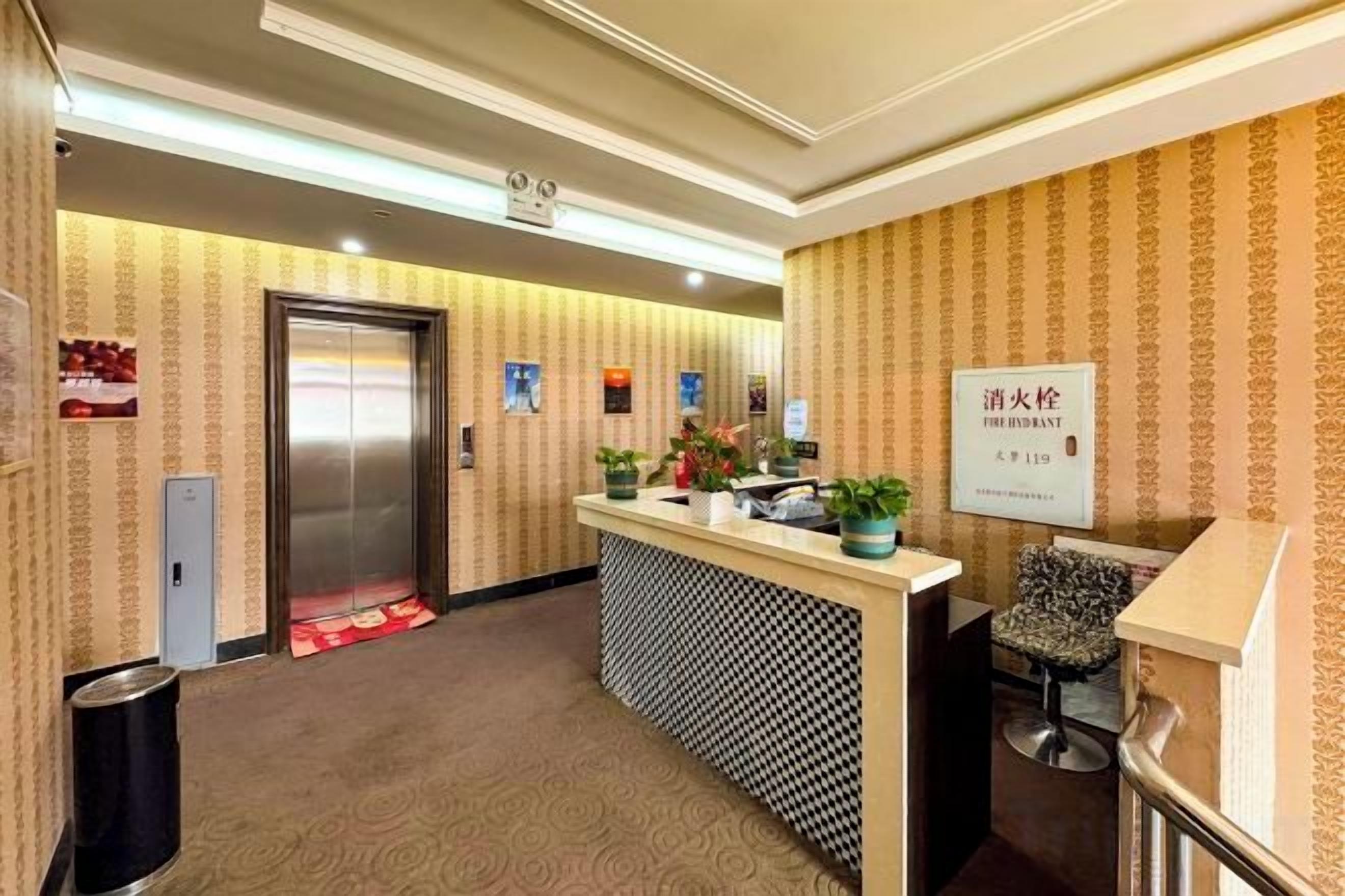 A hotel reception area with a reception desk, a chair, an elevator, and a trash bin.
