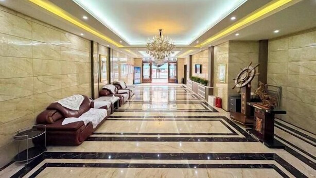 A spacious lobby with a marble floor, leather seating, a chandelier, and a ship's wheel decoration. - Wanliyuan Hotel (Fuyuan)