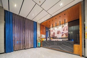 Una zona de recepción de hotel con diseño moderno, que incluye un mostrador de recepción, un ventanal grande y una pared decorativa.