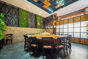 Un salón de conferencias con una mesa redonda, varias sillas y una pared verde con plantas.