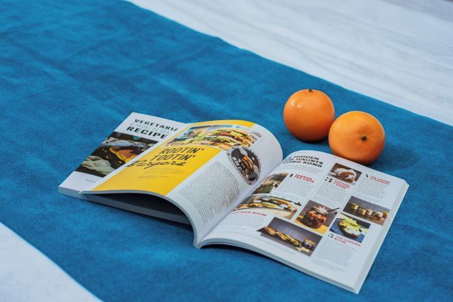 An open magazine on a blue towel with two oranges beside it.