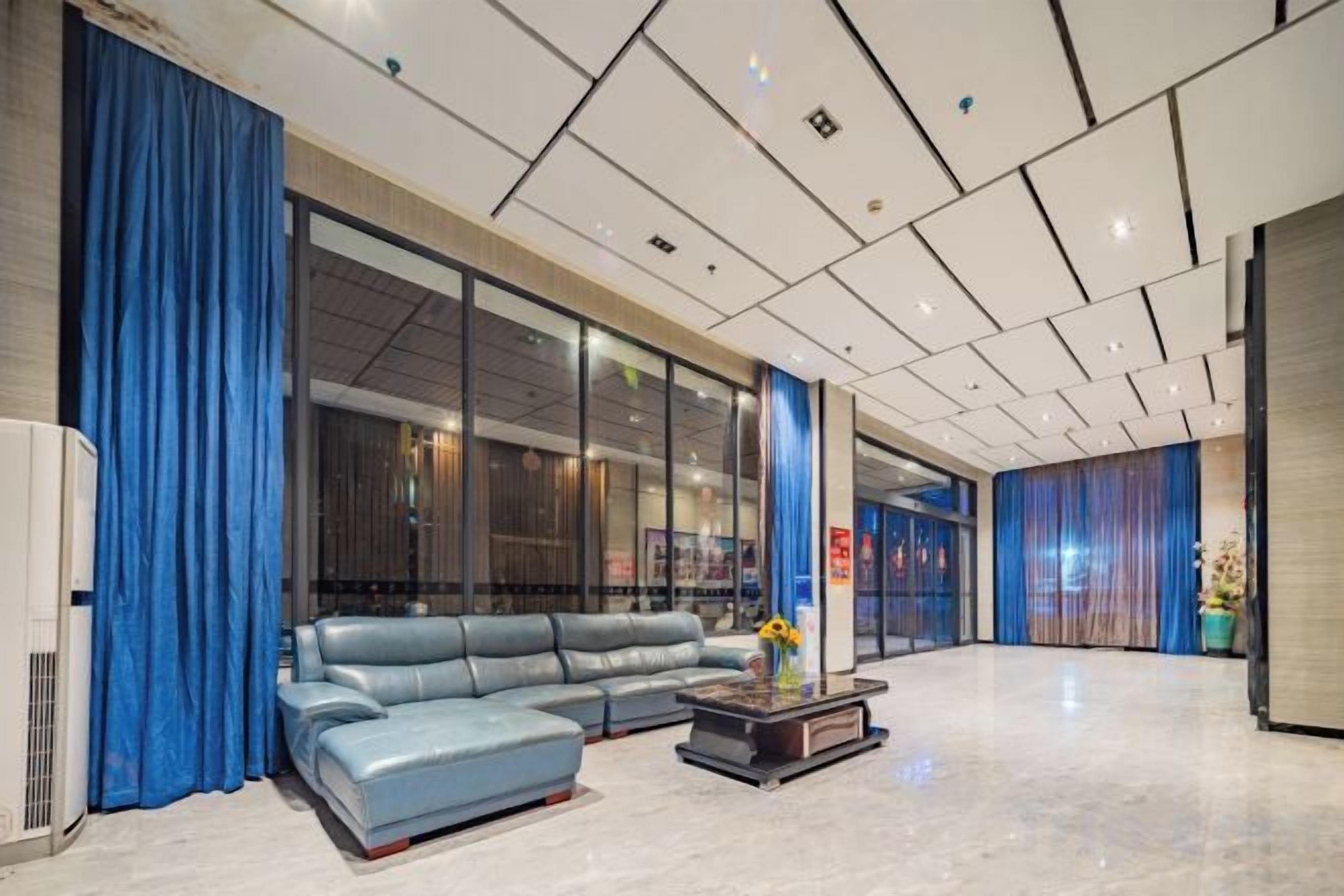 Een moderne lobby met een leren bank, een salontafel en een groot raam met gordijnen.