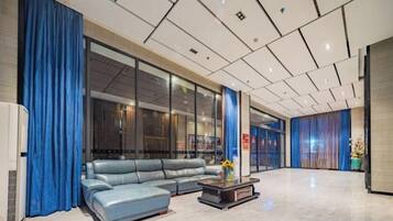Een moderne lobby met een leren bank, een salontafel en een groot raam met gordijnen.