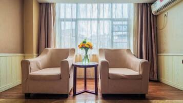 Een kamer met twee beige fauteuils, een kleine ronde tafel met een bloevas en een groot raam met gordijnen.
