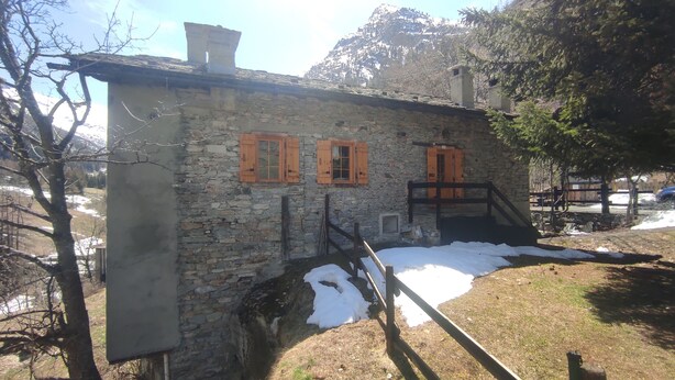 Un edificio de piedra con contraventanas de madera, una chimenea y una pequeña escalera que conduce a un porche.