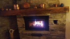 Una chimenea de piedra con un estufa de leña moderna, un estante superior con varias ollas de cobre y una pared de piedra.