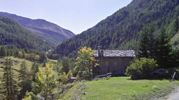 Une maison de campagne en pierre, dotée d’un toit en pente, entourée d’une vallée verdoyante et d’une forêt dense.