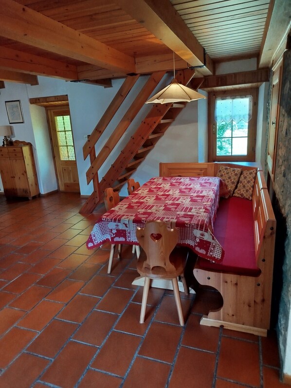 A rustic wooden room with a loft bed, a dining table with chairs, and a staircase.