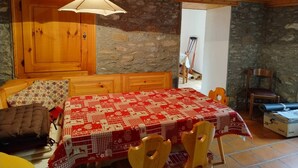 Un comedor acogedor con una mesa y sillas de madera, un mantel estampado y una pared de piedra.