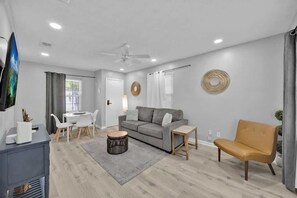 Uma sala de estar moderna com um sofá cinzento, uma poltrona amarela, uma mesa de centro e uma TV sobre um suporte.
