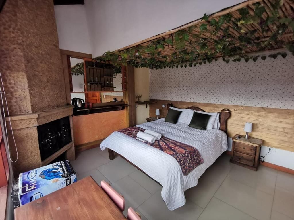 Quarto com cama, cabeceira de madeira, mesa de cabeceira e pequena escrivaninha com cadeira.