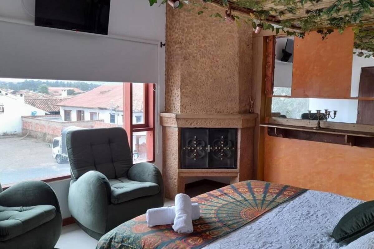 A room with a bed, two armchairs, a fireplace, and a view of the outside.