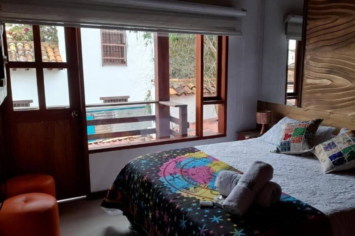 A bedroom with a large window, a bed with colorful bedding, and a wooden headboard.