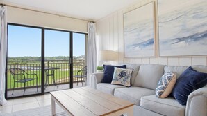 A living room with a sofa, coffee table, and a view of a golf course through a sliding glass door.