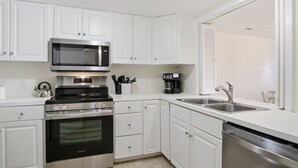A modern kitchen with white cabinetry, a stainless steel microwave, a built-in oven, a coffee maker, and a dishwasher.