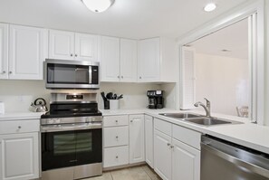 A modern kitchen with white cabinetry, a stainless steel microwave, a built-in oven, a coffee maker, and a dishwasher.