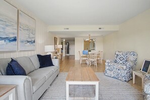 A living room with a sofa, armchair, coffee table, and a dining area with chairs and a table.